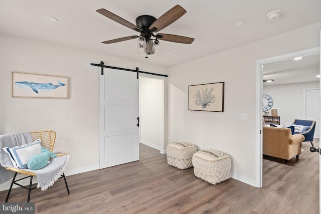 sitting room featuring ceiling fan, a barn door, baseboards, and light wood finished floors