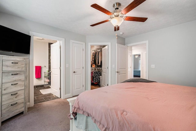 carpeted bedroom featuring connected bathroom, a closet, ceiling fan, a walk in closet, and baseboards