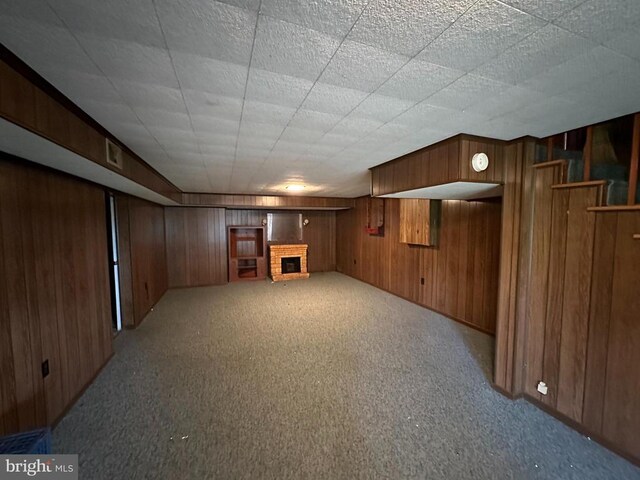 basement featuring light carpet, a fireplace, and wood walls