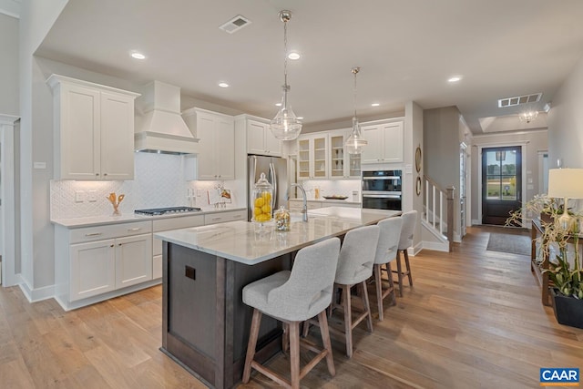 kitchen with stainless steel appliances, white cabinets, premium range hood, and visible vents