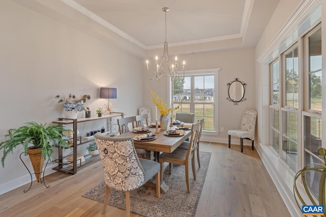 dining space featuring baseboards, light wood-style floors, ornamental molding, a tray ceiling, and an inviting chandelier