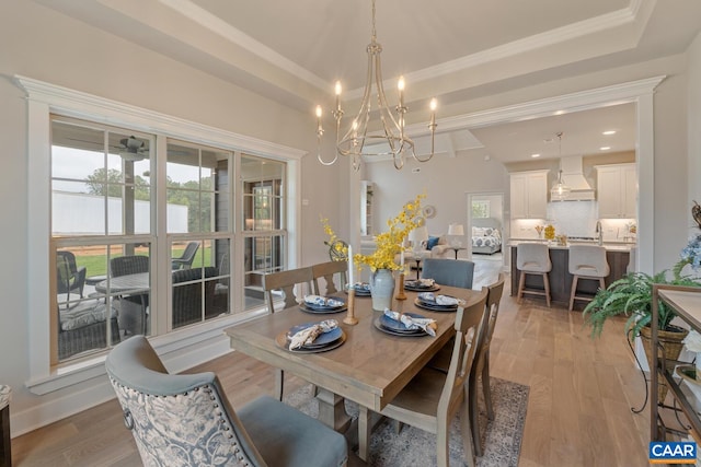 dining area with light wood finished floors, ornamental molding, and a raised ceiling