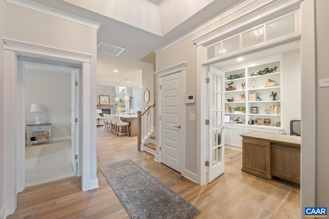 interior space with visible vents, built in features, light wood-style flooring, ornamental molding, and stairs