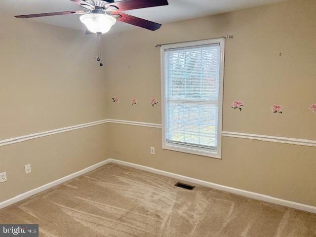 carpeted spare room featuring visible vents, baseboards, and a ceiling fan