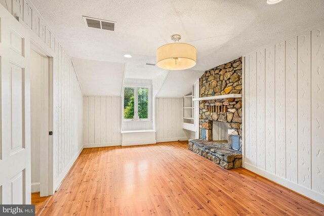 unfurnished living room featuring hardwood / wood-style flooring, lofted ceiling, a fireplace, and a textured ceiling