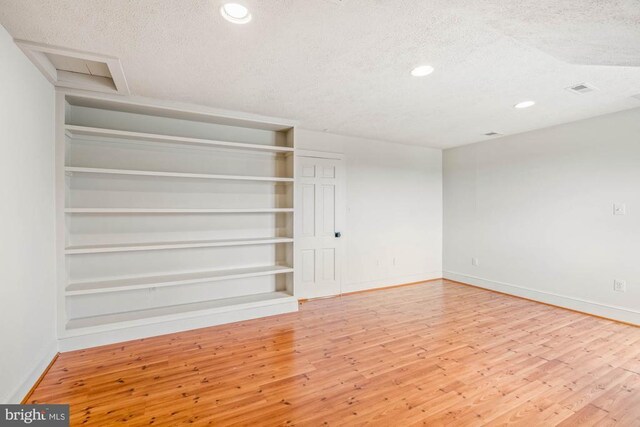 unfurnished living room with hardwood / wood-style flooring, built in shelves, and a textured ceiling