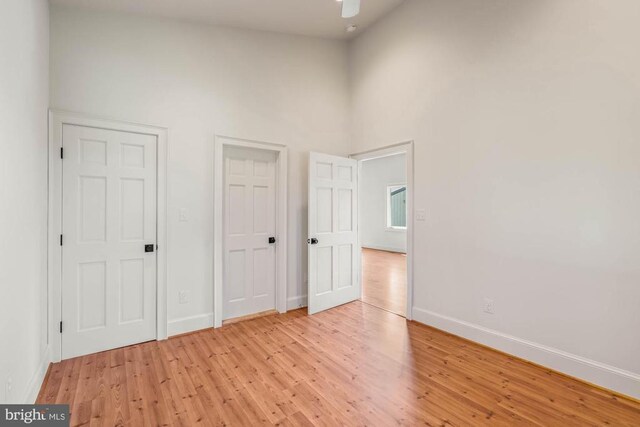 unfurnished bedroom featuring ceiling fan, a high ceiling, and light wood-type flooring