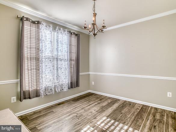 unfurnished dining area featuring an inviting chandelier, hardwood / wood-style floors, crown molding, and a healthy amount of sunlight