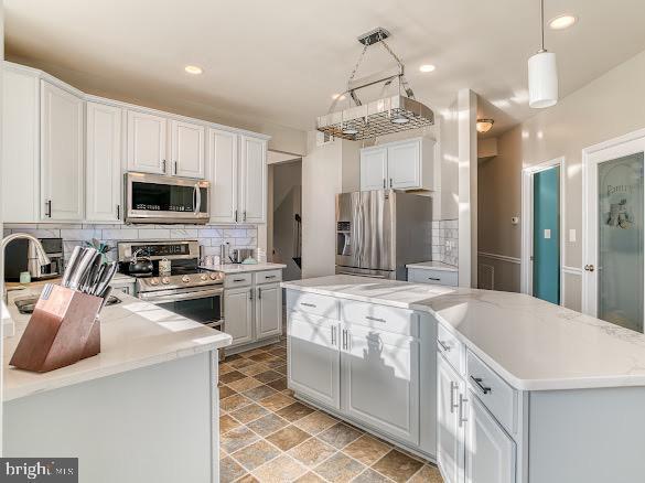 kitchen with appliances with stainless steel finishes, white cabinetry, tasteful backsplash, a kitchen island, and decorative light fixtures