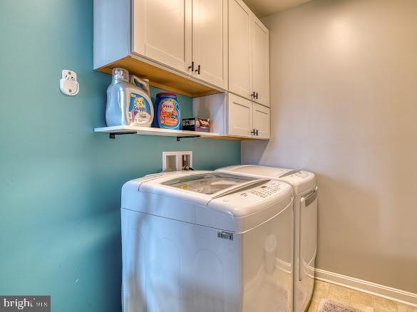 clothes washing area with separate washer and dryer and cabinets