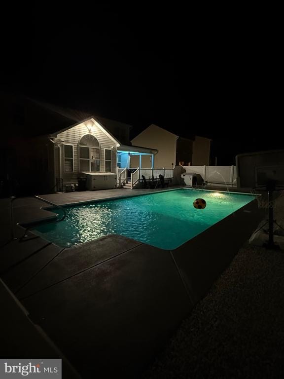 pool at night with an outbuilding, a patio, and pool water feature