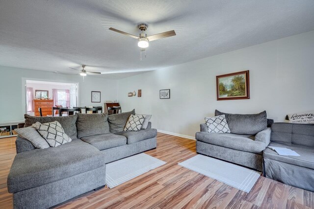 living room with ceiling fan, a textured ceiling, and light wood-type flooring