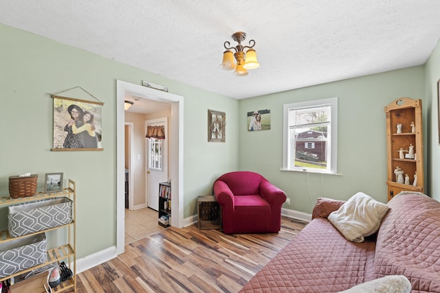 living area with baseboards, a textured ceiling, a notable chandelier, and wood finished floors
