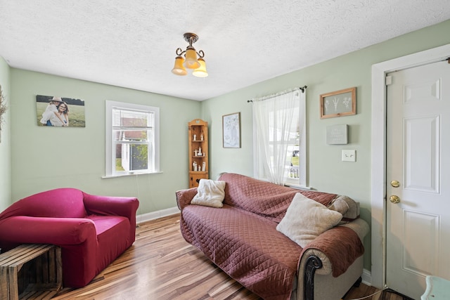 living room with an inviting chandelier, baseboards, a textured ceiling, and wood finished floors