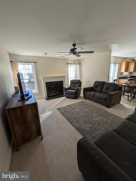 living area with light carpet, a fireplace, and a ceiling fan