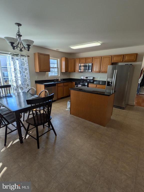 kitchen featuring stainless steel appliances, a center island, brown cabinets, dark countertops, and pendant lighting