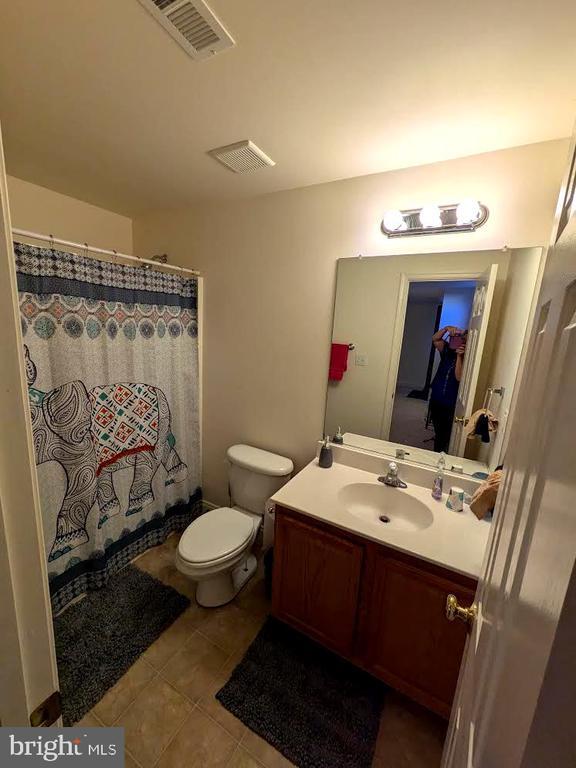 bathroom with visible vents, toilet, curtained shower, tile patterned flooring, and vanity