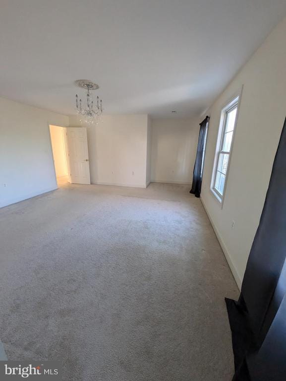 empty room with light colored carpet and a notable chandelier