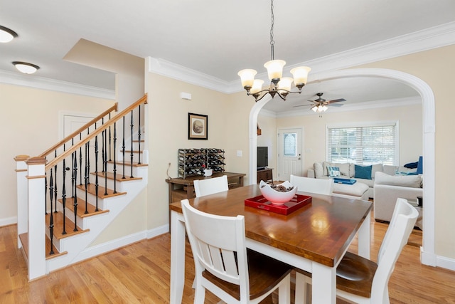 dining space with arched walkways, ceiling fan with notable chandelier, light wood-style floors, and ornamental molding