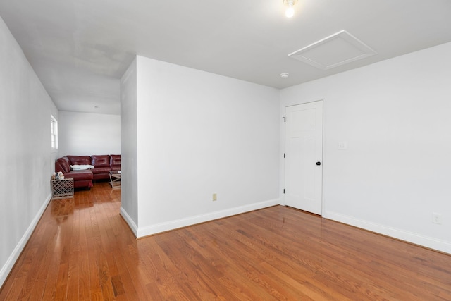 empty room with attic access, baseboards, and wood finished floors