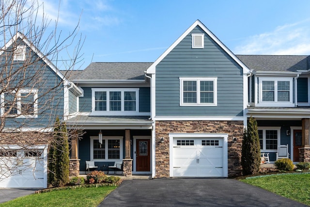 view of front of property featuring roof with shingles, covered porch, a garage, stone siding, and aphalt driveway