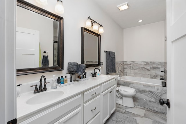 bathroom featuring tiled bath, double vanity, toilet, and a sink