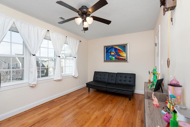 living area featuring a ceiling fan, baseboards, visible vents, and light wood finished floors