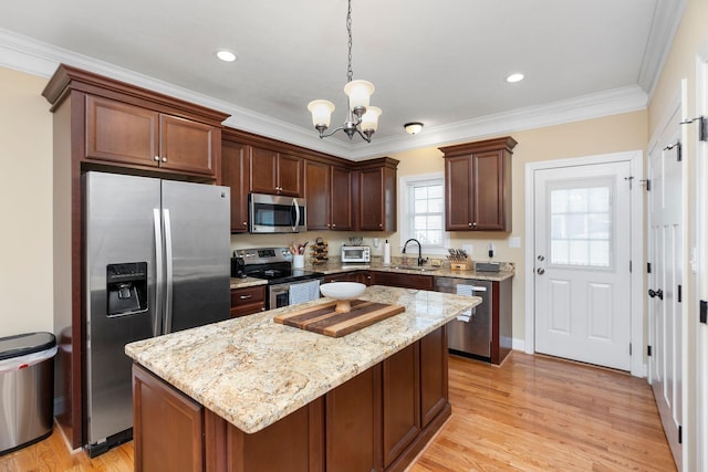 kitchen featuring light wood-type flooring, ornamental molding, appliances with stainless steel finishes, an inviting chandelier, and a sink