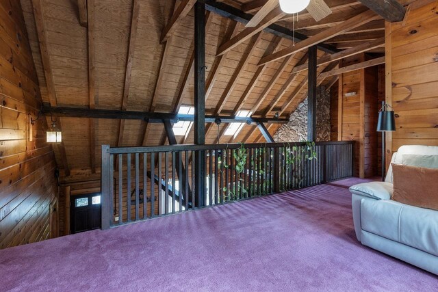 interior space with carpet floors, vaulted ceiling with beams, ceiling fan, and wood walls