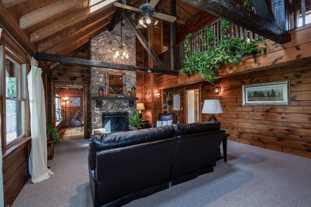 living room featuring wooden walls, carpet floors, beamed ceiling, ceiling fan, and a fireplace