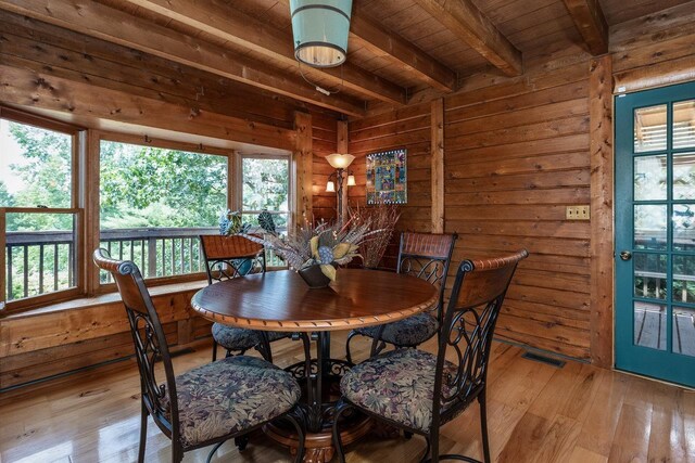 dining space with light hardwood / wood-style flooring, wooden walls, and beamed ceiling