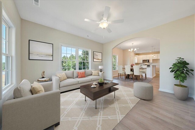 living room with ceiling fan with notable chandelier and light hardwood / wood-style floors