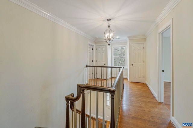 corridor with light wood finished floors, baseboards, ornamental molding, an inviting chandelier, and an upstairs landing