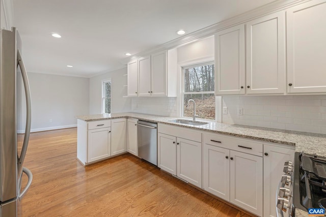 kitchen featuring a peninsula, a sink, white cabinets, appliances with stainless steel finishes, and light wood-type flooring