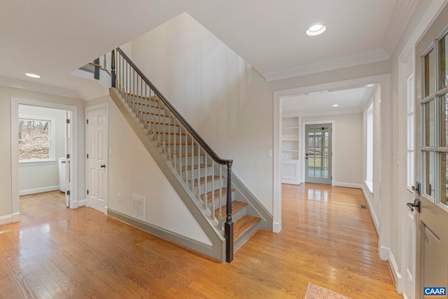 foyer entrance featuring ornamental molding, baseboards, visible vents, and light wood finished floors