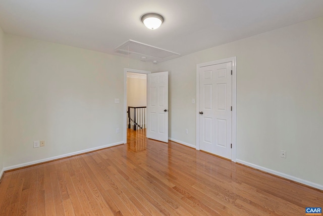 spare room with attic access, light wood-style flooring, and baseboards