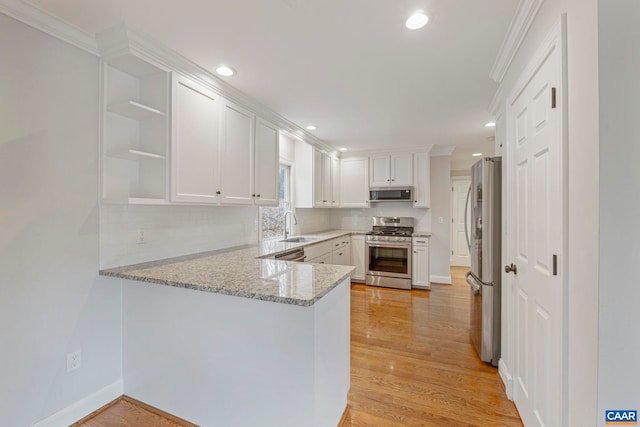 kitchen with a peninsula, light wood-style floors, appliances with stainless steel finishes, and a sink