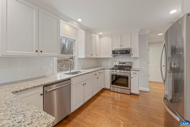 kitchen featuring light stone counters, stainless steel appliances, a sink, white cabinetry, and light wood finished floors