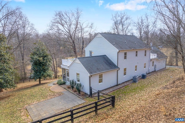 exterior space with a yard, central AC unit, roof with shingles, and fence private yard