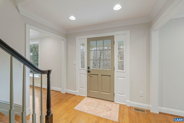 foyer with ornamental molding, visible vents, light wood-style flooring, and baseboards