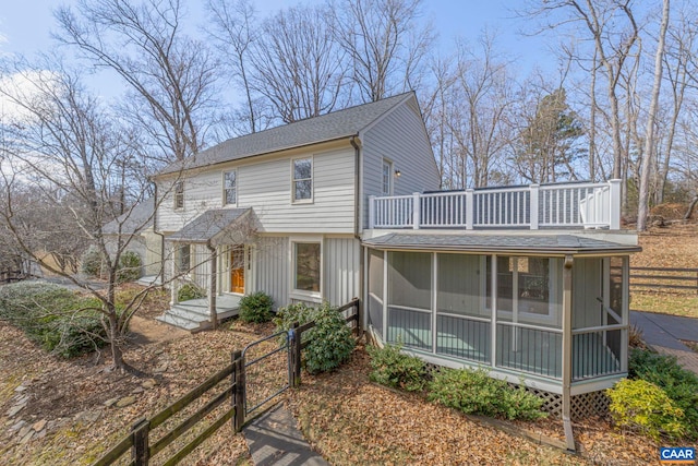 view of front of home with roof with shingles, fence, and a sunroom