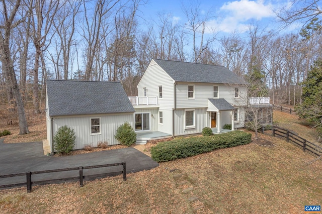 view of front of home with aphalt driveway, a shingled roof, fence, and a balcony