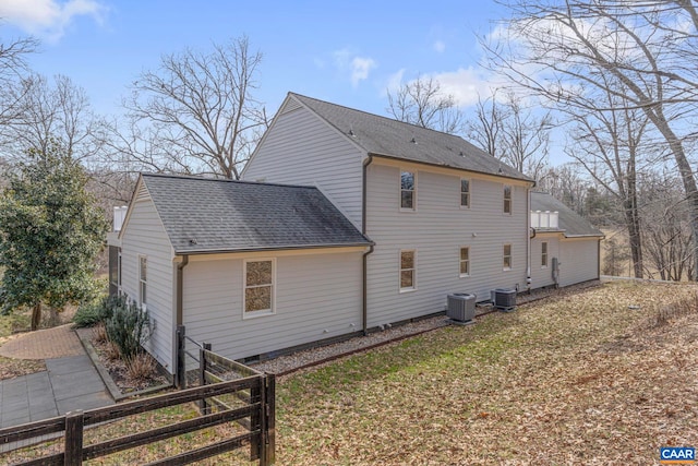 exterior space with a yard, fence, central AC unit, and roof with shingles