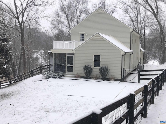 snow covered rear of property featuring fence and a balcony