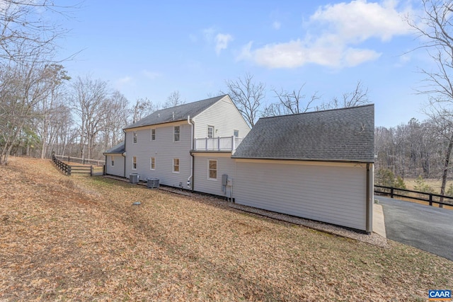 rear view of house with a shingled roof, fence, a balcony, and central air condition unit