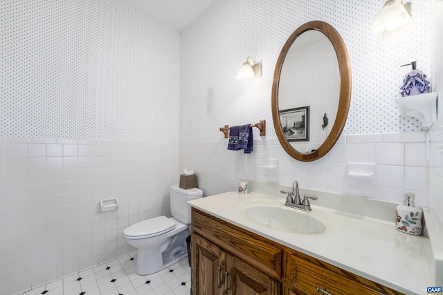 bathroom featuring tile patterned floors, toilet, tile walls, wallpapered walls, and vanity