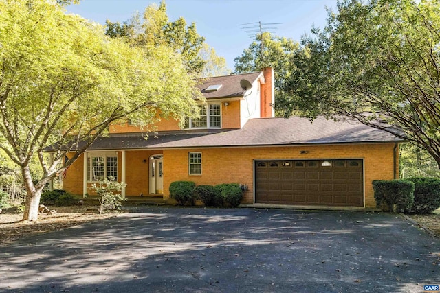 view of front of home featuring aphalt driveway, brick siding, a chimney, and an attached garage