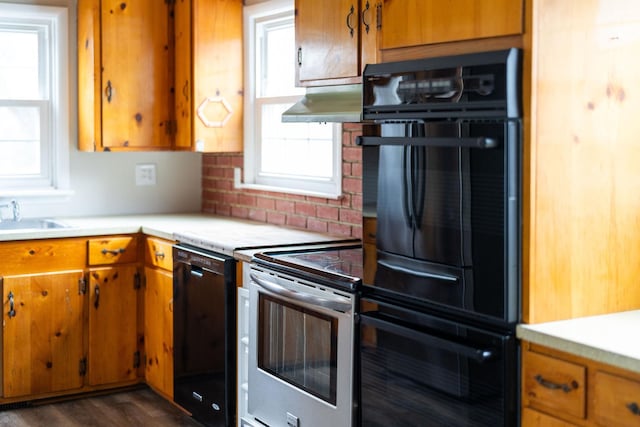 kitchen featuring brown cabinetry, light countertops, under cabinet range hood, and black appliances