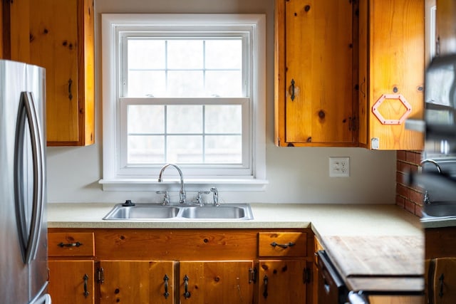 kitchen featuring light countertops, a sink, freestanding refrigerator, and brown cabinets