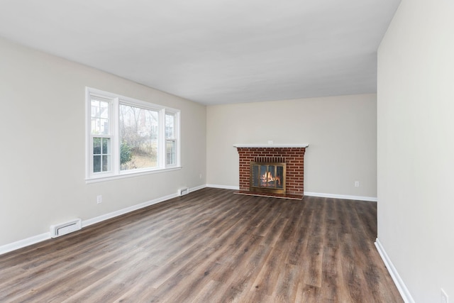 unfurnished living room with a baseboard heating unit, a brick fireplace, wood finished floors, and baseboards